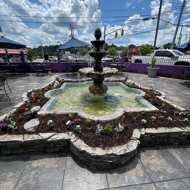 Decorative fountain surrounded by flowers, stone, and a paved patio