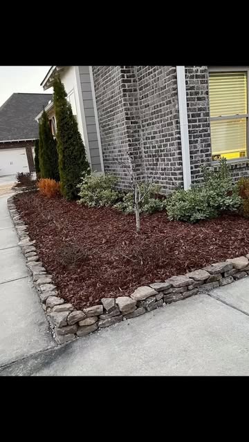 Fresh dark mulch bed with shrubs and a natural stone border
